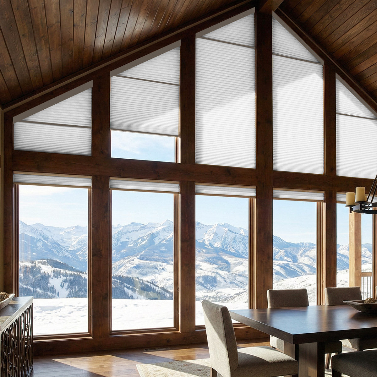 White light filtering trapezoid cellular shades in the timber gable of a mountain cabin great room above a dining table