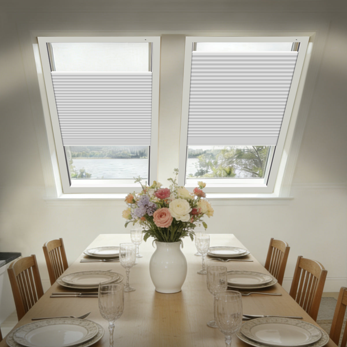 Two white top-down bottom-up blackout cellular shades on sloped skylights above a dining table set with flowers