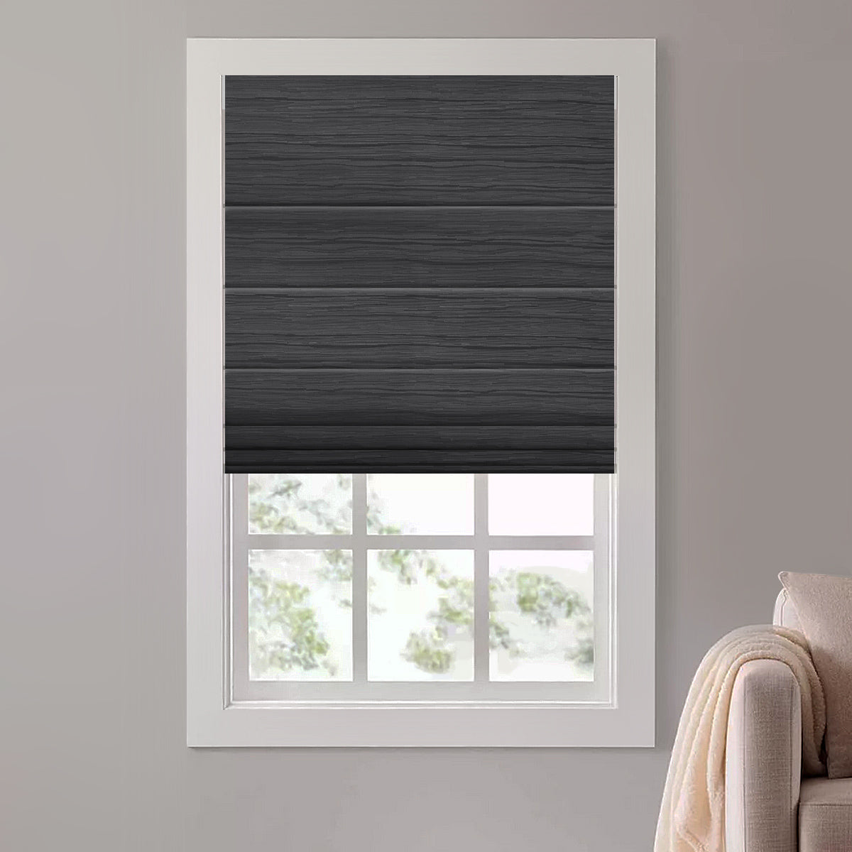 Black blackout motorized roman shade with flat folds lowered over a window beside a cozy blush armchair