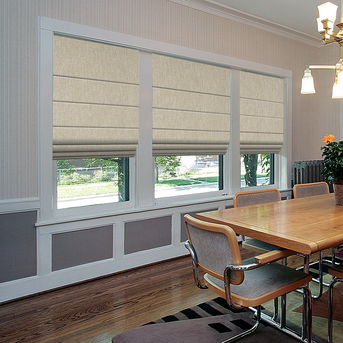Cream motorized roman shades half raised over three dining room windows above a wooden table and chairs