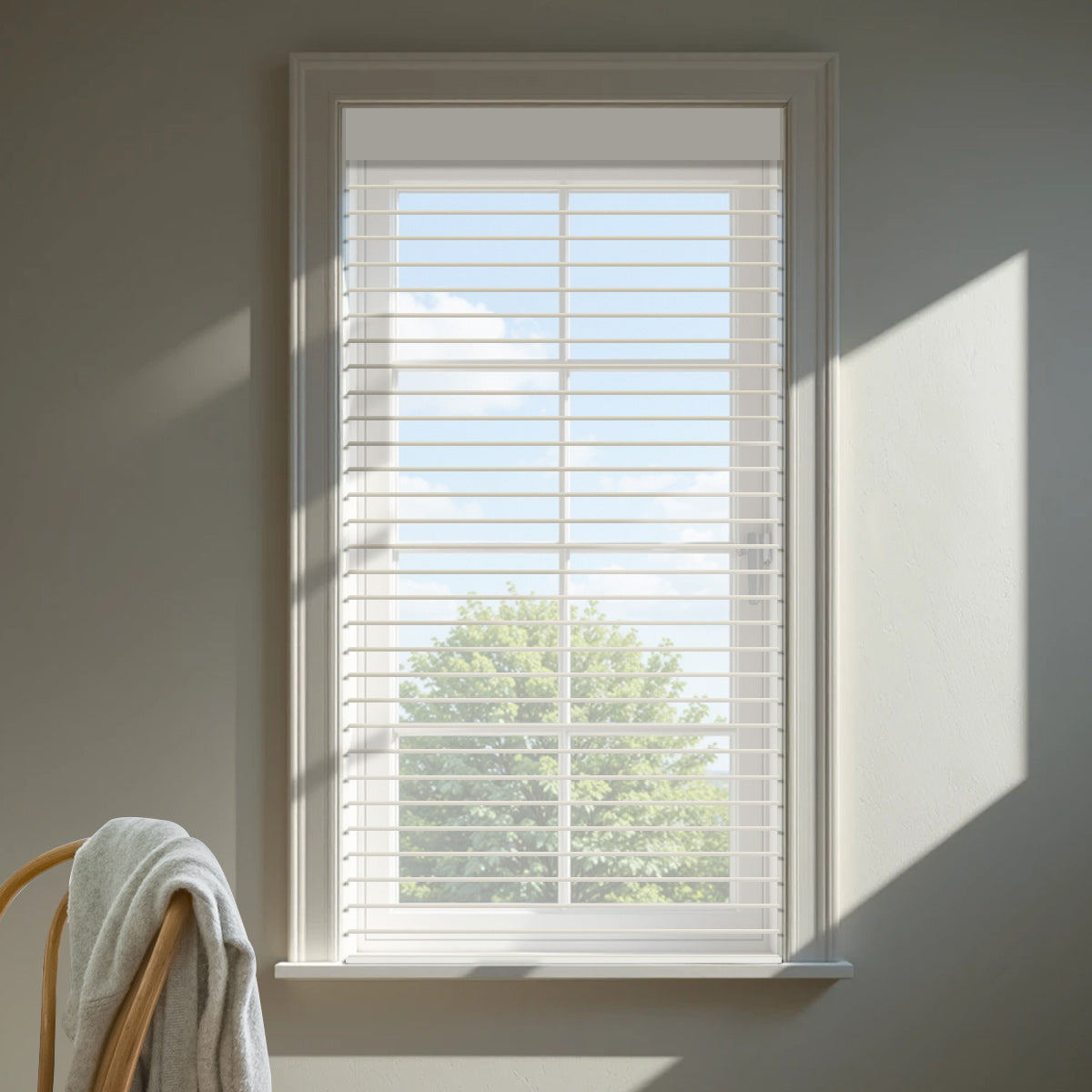 Cream light filtering sheer shade lowered on a sunlit window casting soft shadows on a grey wall