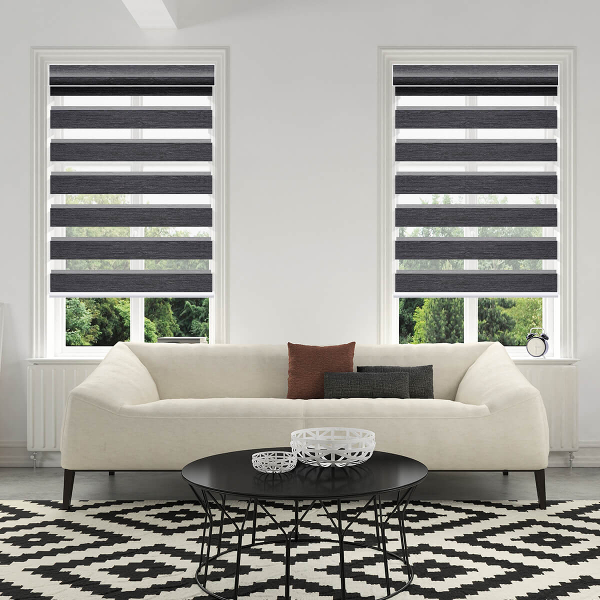 Graphite motorized zebra shades on two tall windows behind a white sofa and black-and-white patterned rug in a bright living room