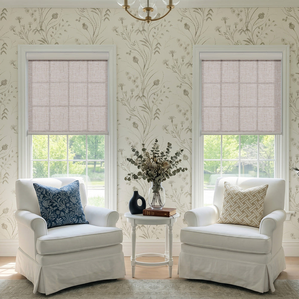 Caramel linen-texture roller shades on two windows in a sitting room with floral wallpaper and white armchairs